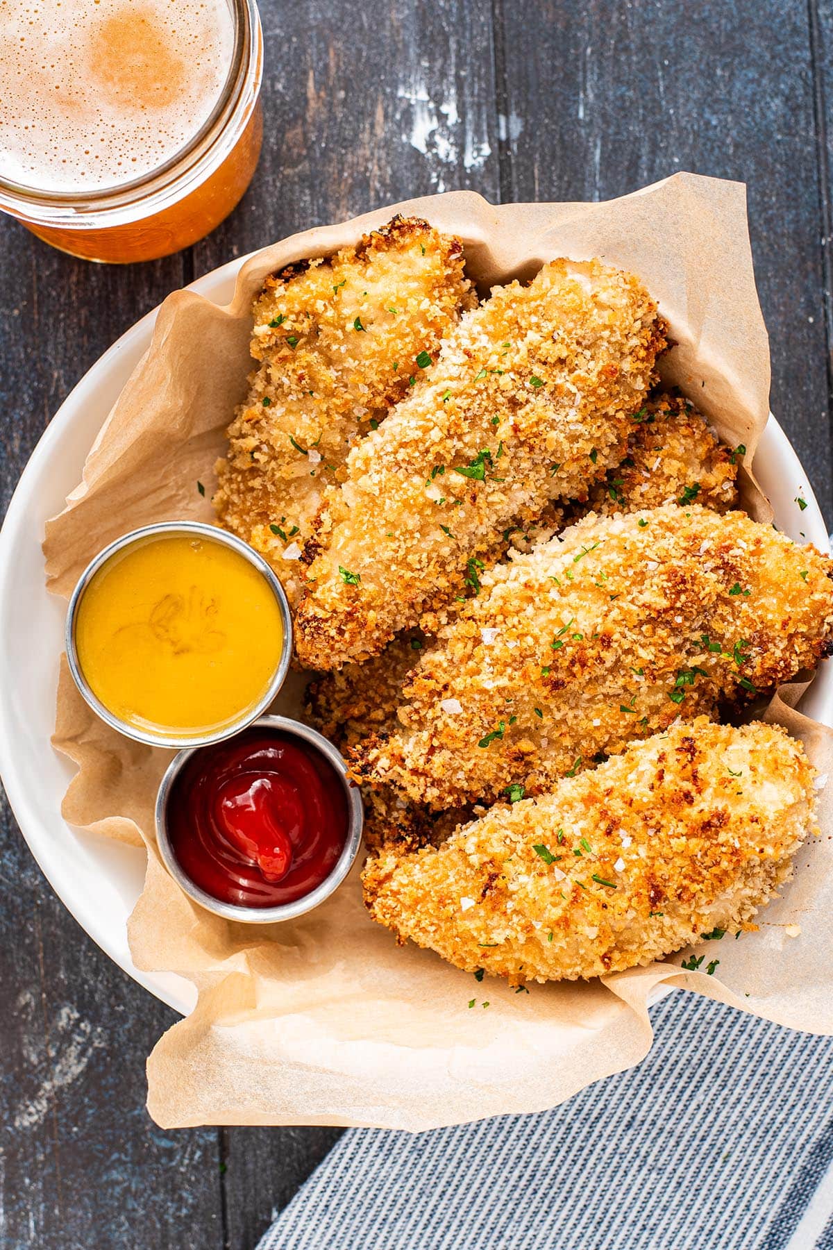 Golden baked chicken tenders coated in panko crumbs in a shallow bowl served with honey mustard and ketchup.