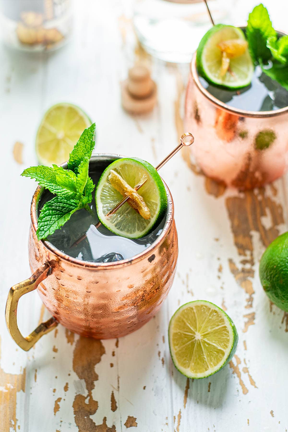 Two Tequila Mule cocktails served in copper mugs garnished with mint leaves, a lime wheel, and candied ginger.