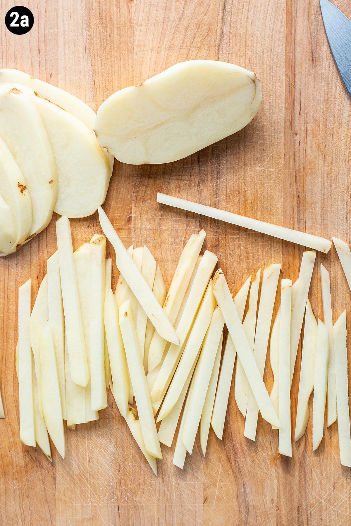 Hand cut, uncooked French fries on a wooden cutting board.