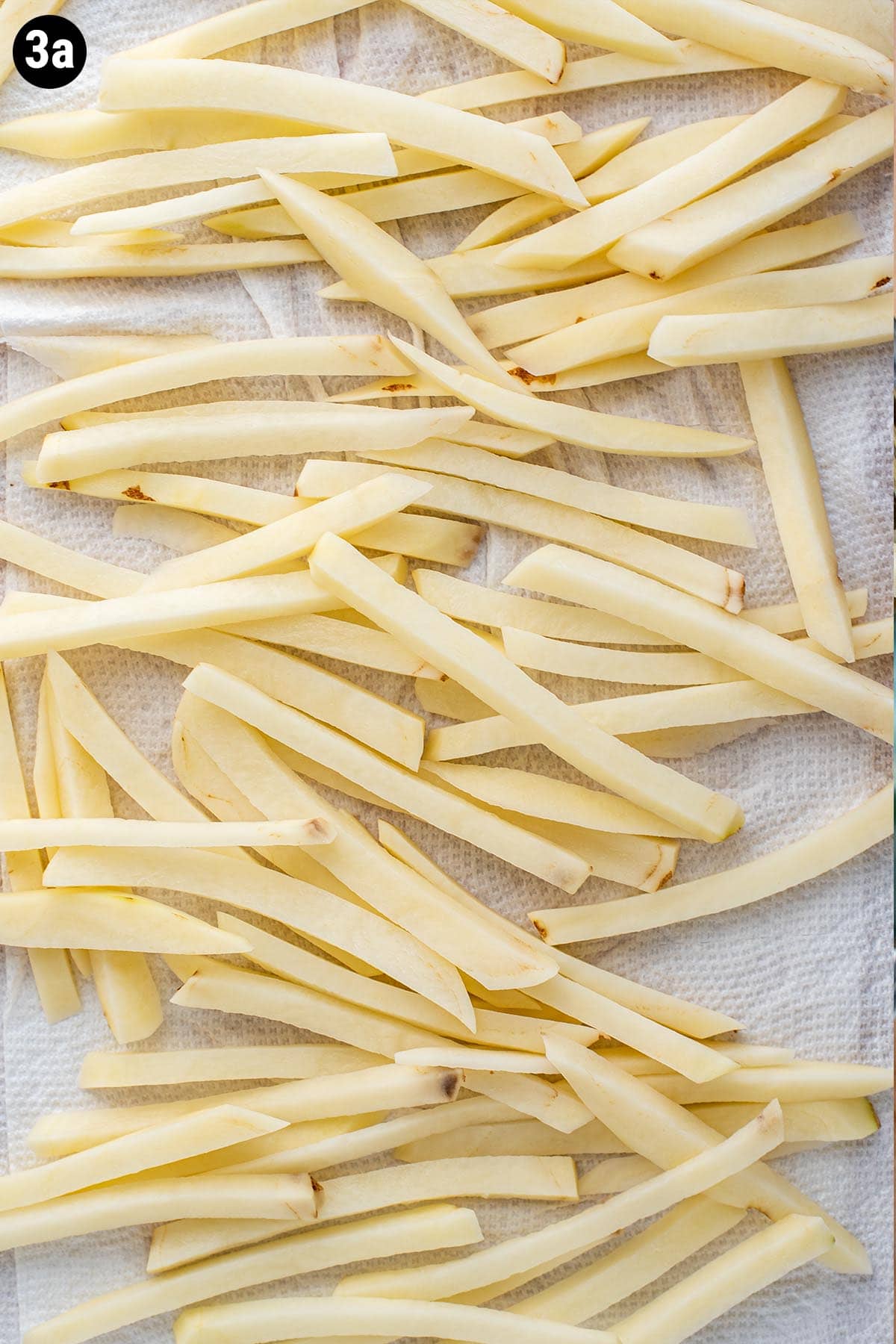 Uncooked hand cut French fries drying on paper towel after soaking in water.