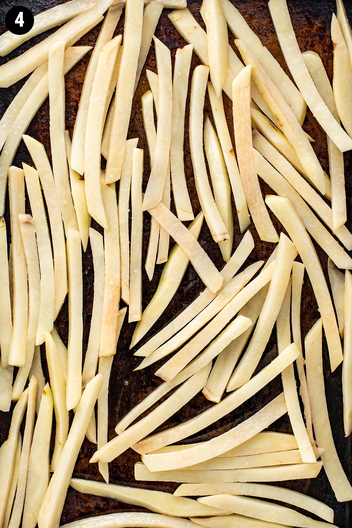 Uncooked French fries layered on a baking sheet before baking.