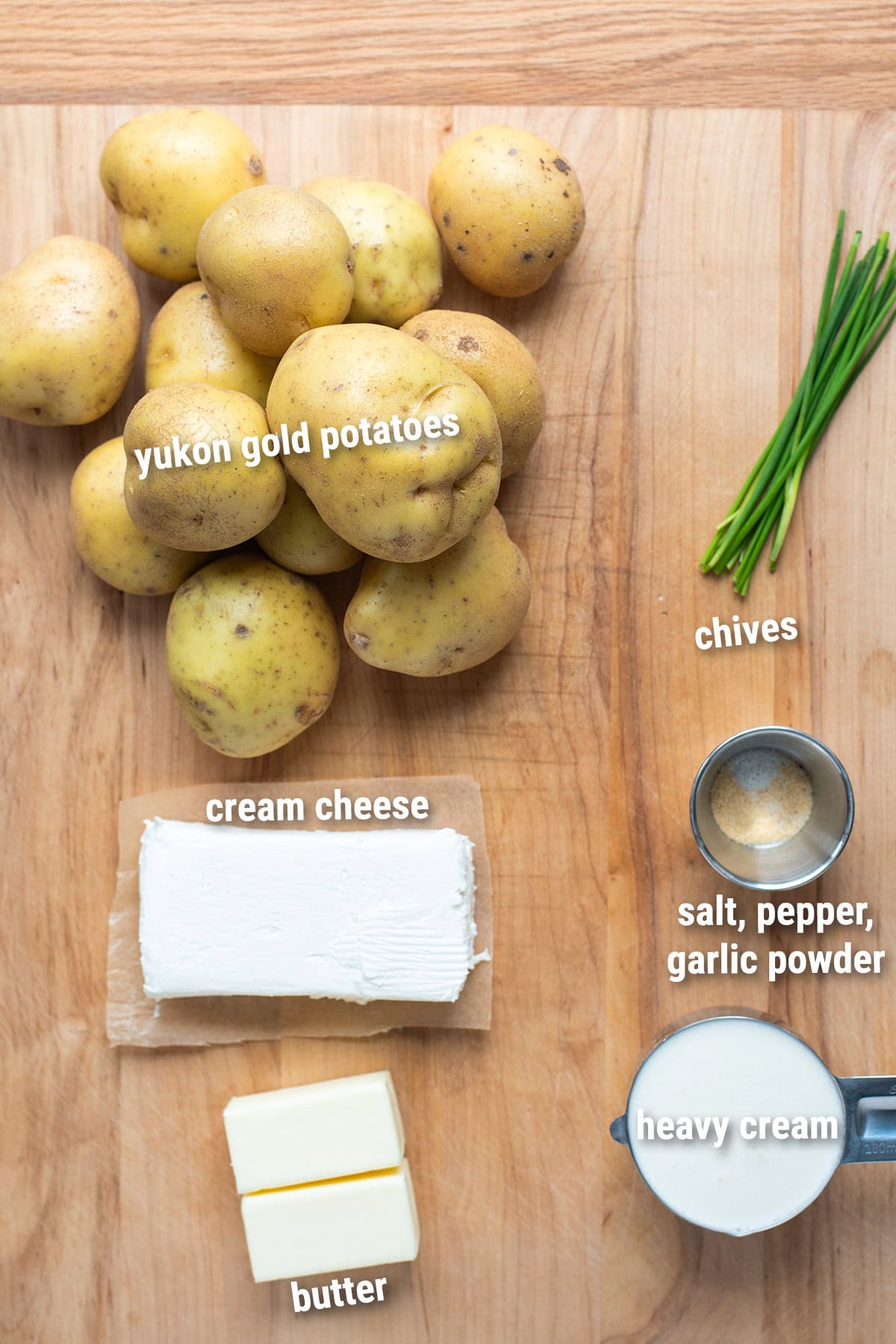 Raw, uncooked mashed potatoes ingredients laid out on a wooden cutting board.