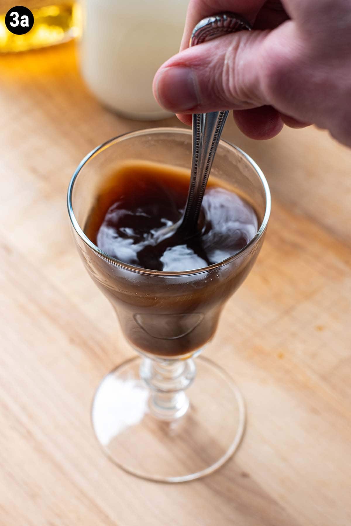 A hand stirring hot coffee and sugar together while making an Irish Coffee.