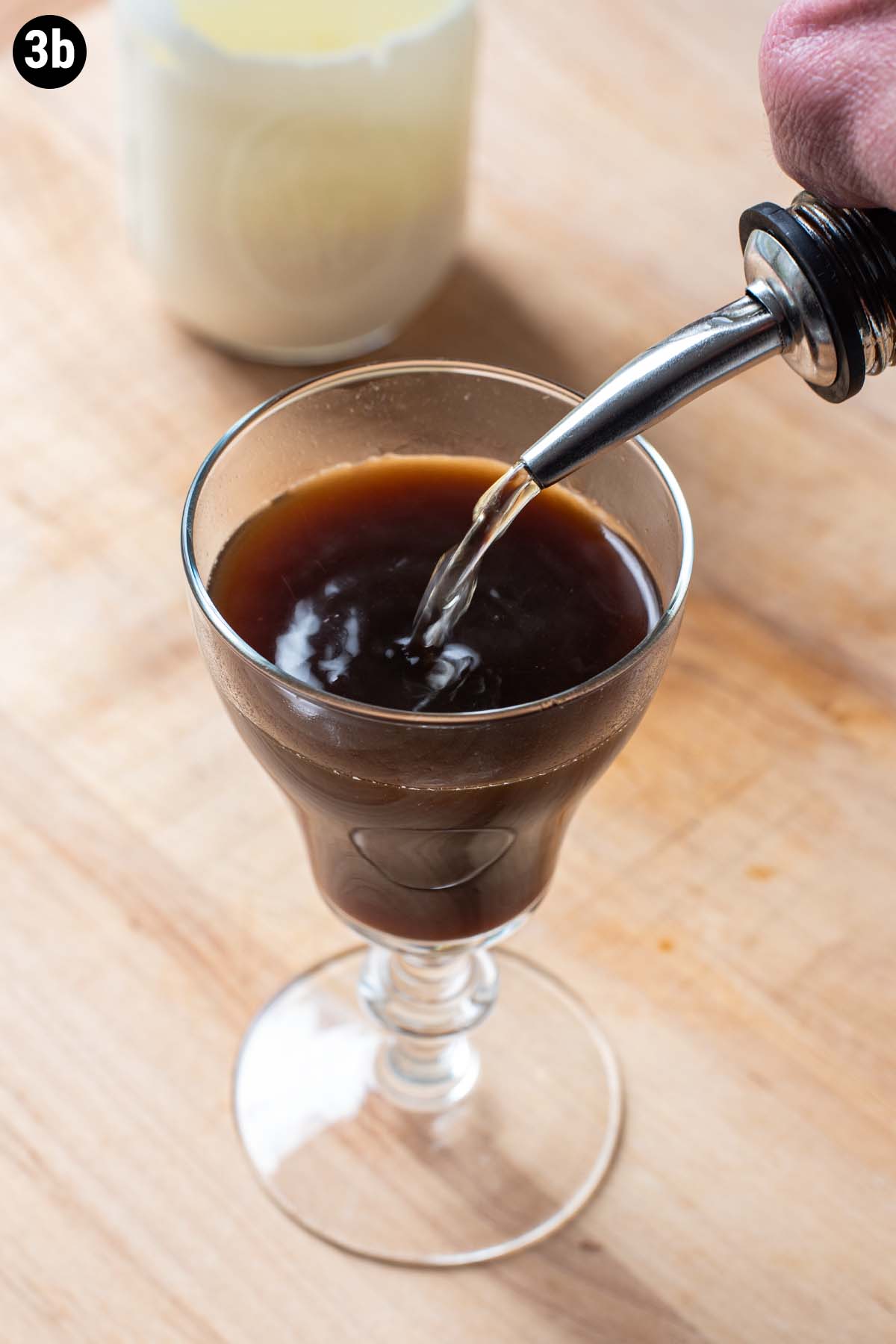 A hand pouring Irish Whiskey into an Irish Coffee through a speed pourer.