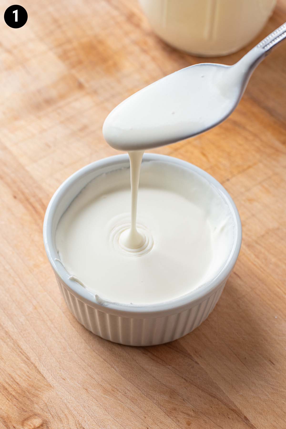 A spoon lifting out of a small white dish of lightly whipped cream.