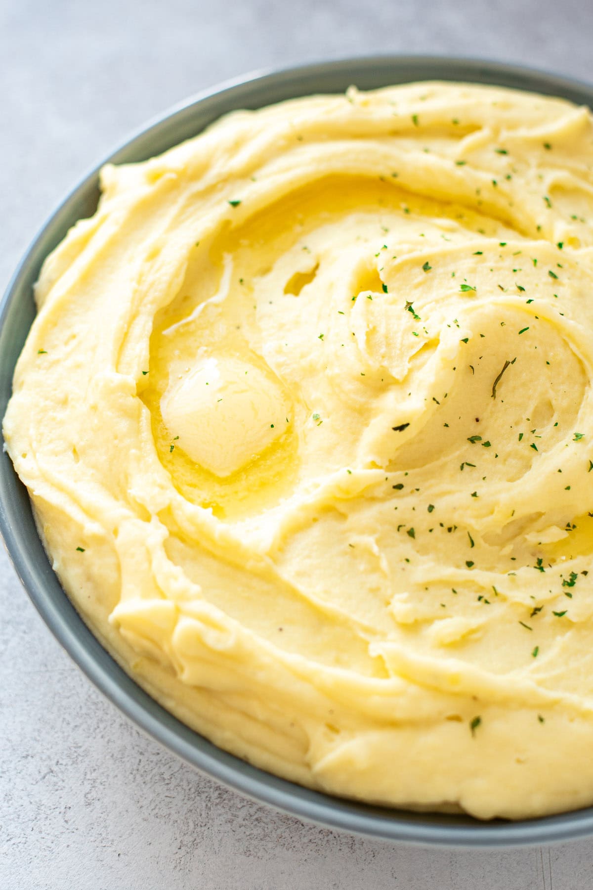 Golden mashed potatoes in a shallow bowl topped with melted butter and fresh parsley.