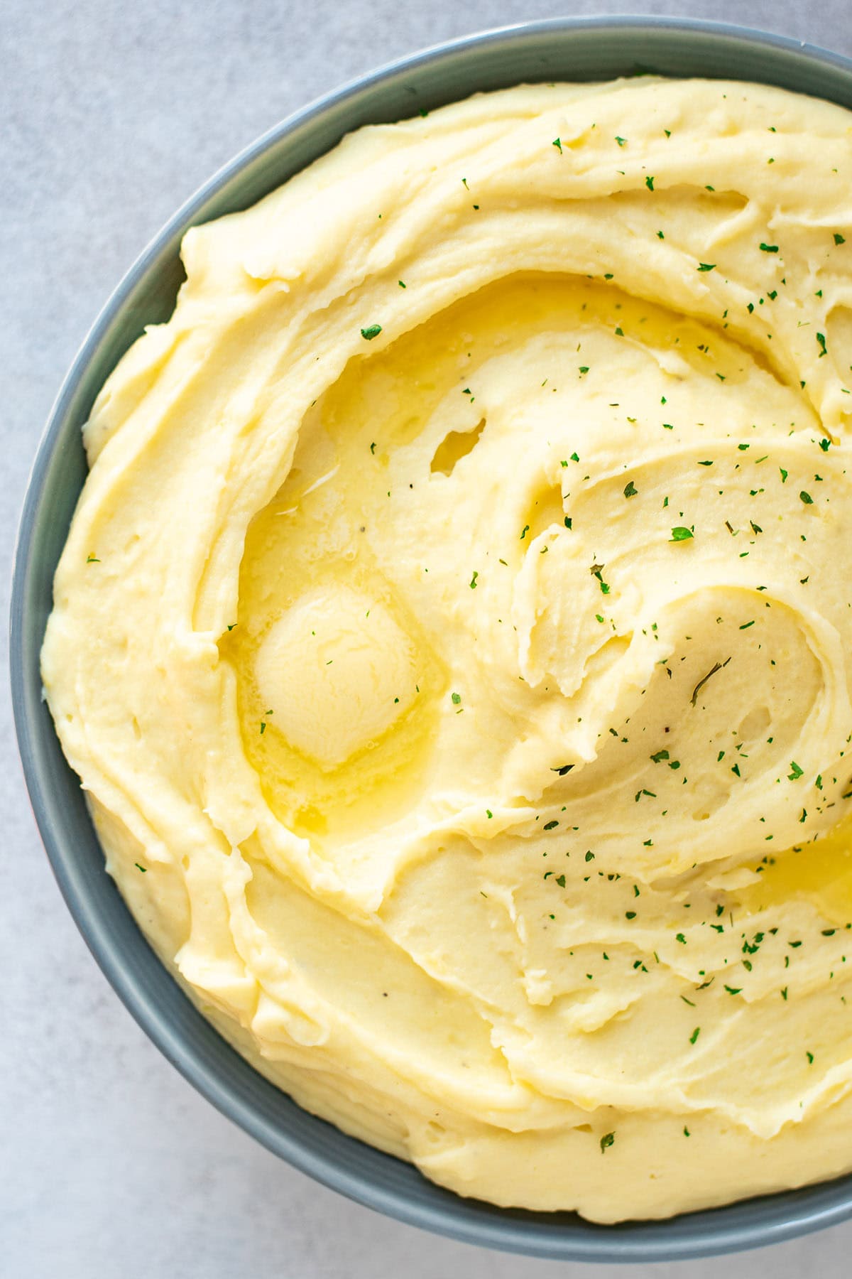 Golden cream cheese mashed potatoes in a bowl topped with melting butter and fresh chopped parsley.