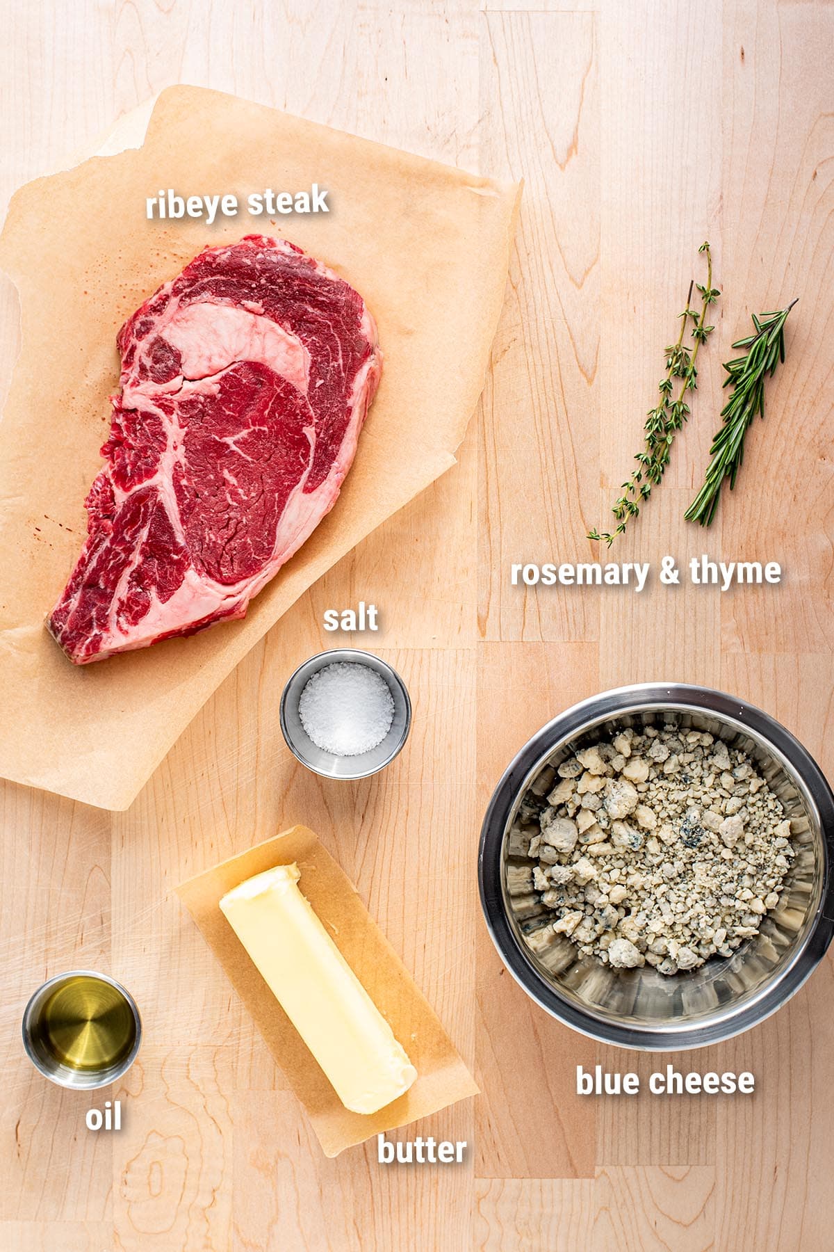 Raw, uncooked ingredients for cooking ribeye steak on a wooden cutting board.