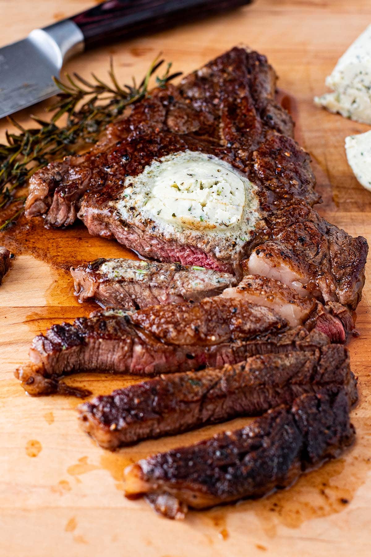 A pan seared medium cooked steak sliced on a cutting board topped with blue cheese compound butter.
