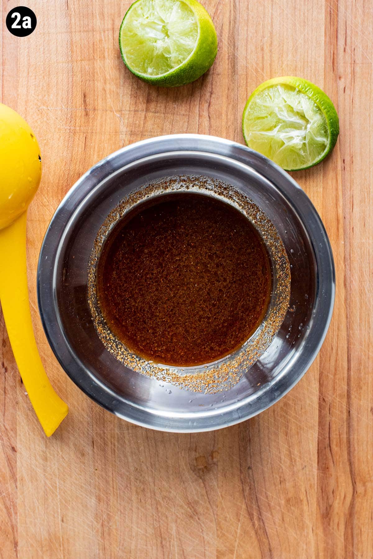 A simple steak marinade made with olive oil , fresh limes, and spices in a small metal bowl.