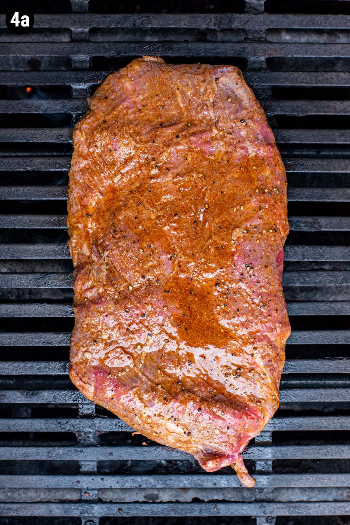 An uncooked seasoned flank steak cooking on the grill.