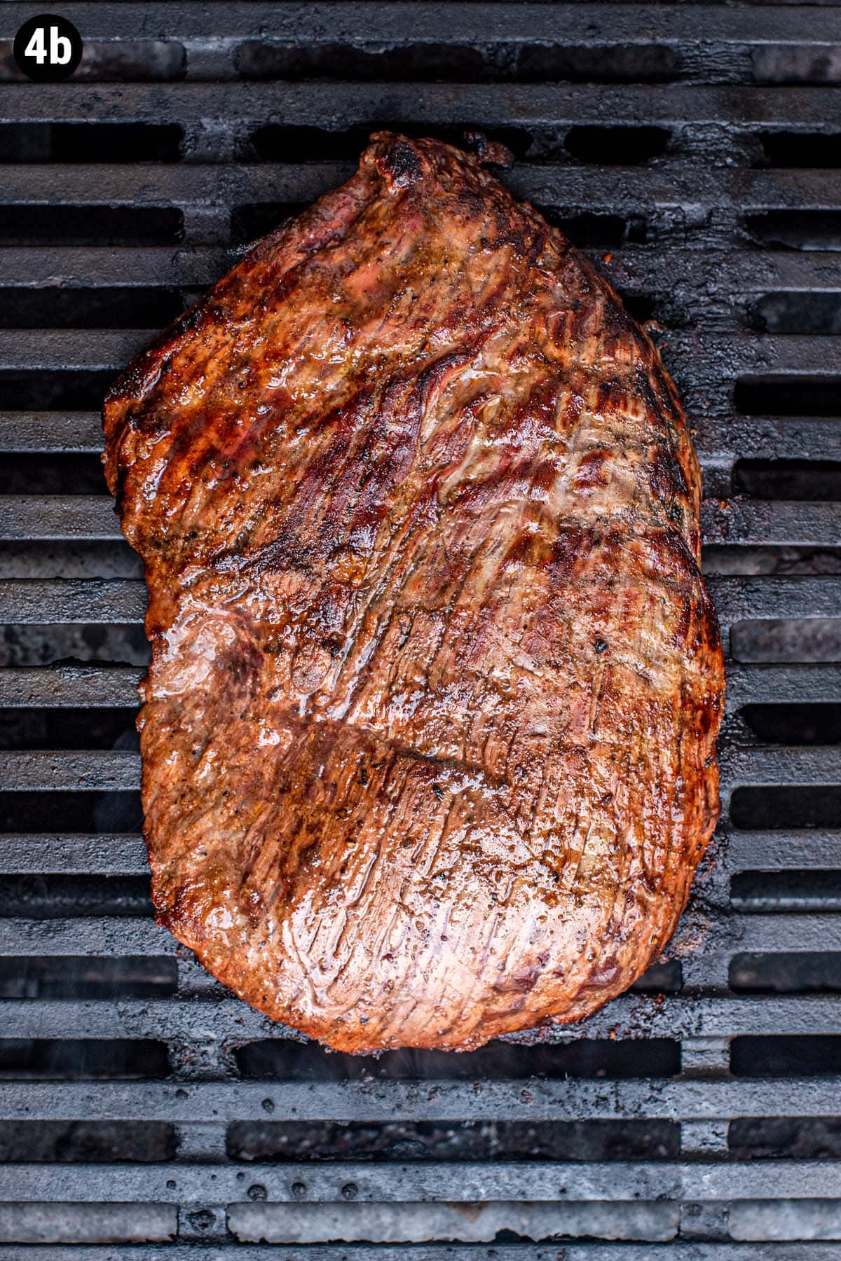 A caramelized, seared, flank steak cooking on a grill.