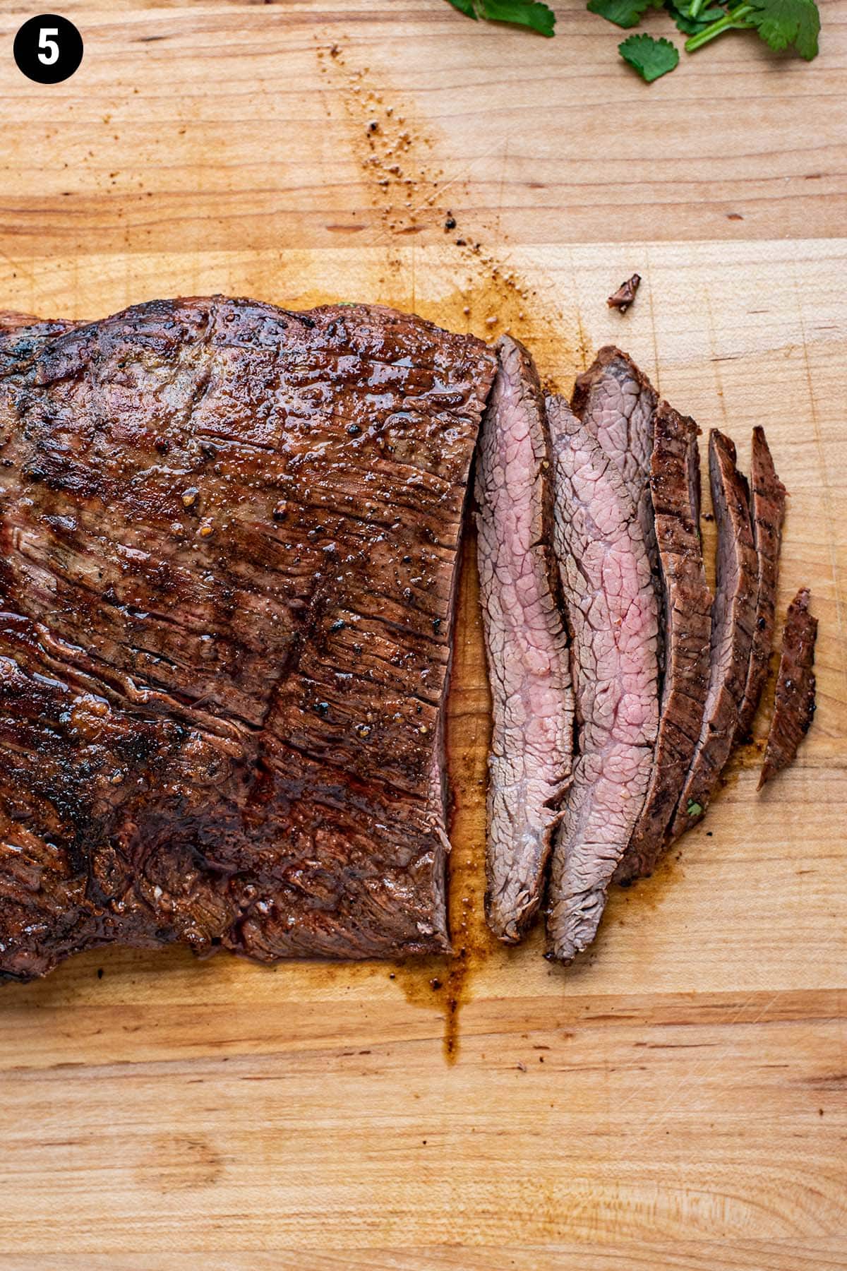 Grilled sliced flank steak with a pink center on a wooden cutting board.