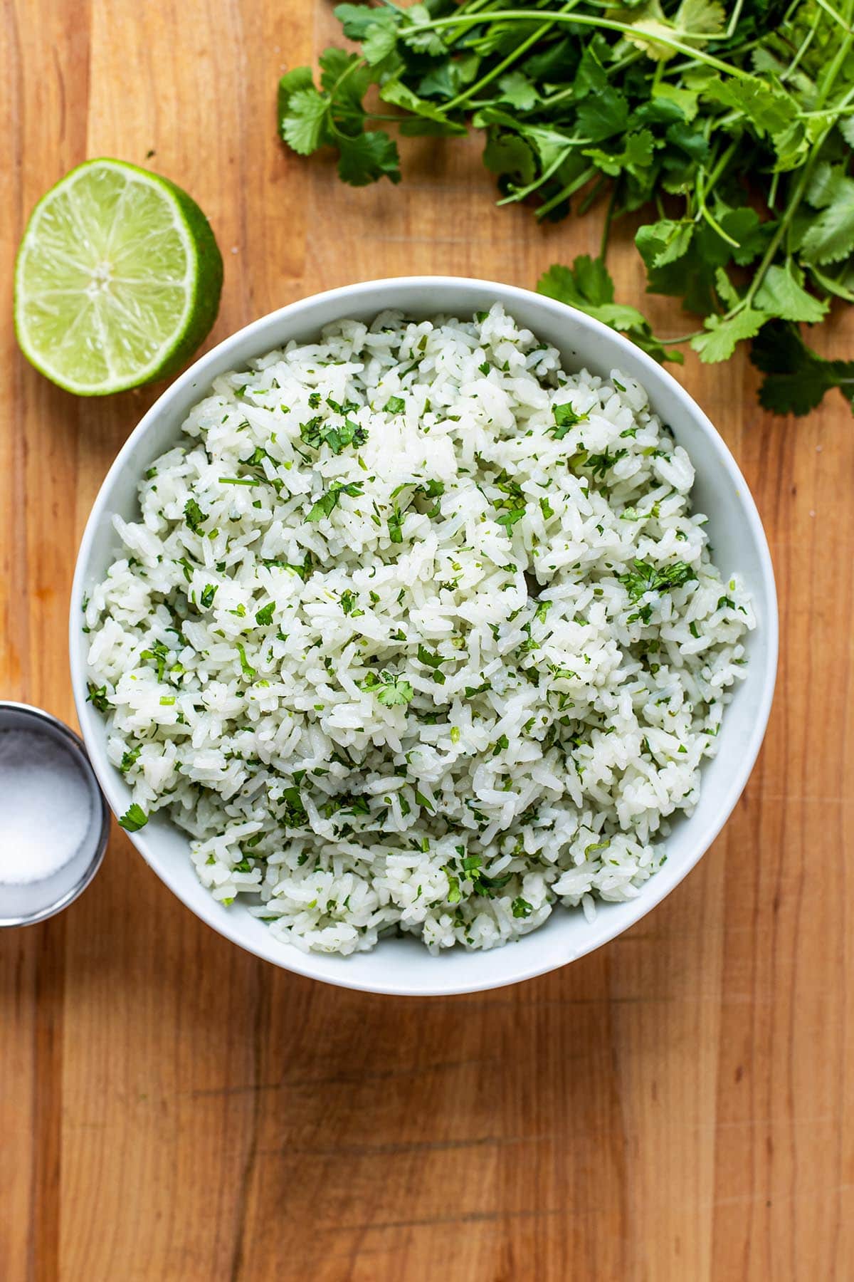 Cilantro lime rice made with white rice in a bowl on a cutting board with a halved lime and fresh cilantro.