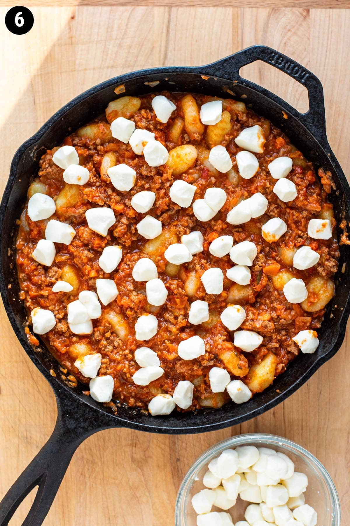 Gnocchi in a cast iron skillet in a bolognese sauce topped with mozzarella balls.