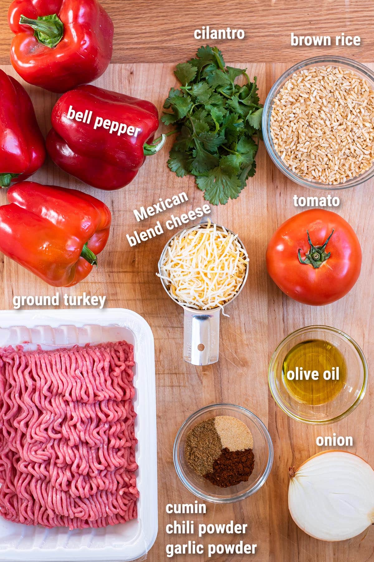 Raw, uncooked ground turkey stuffed peppers ingredients laid out on a wooden cutting board.