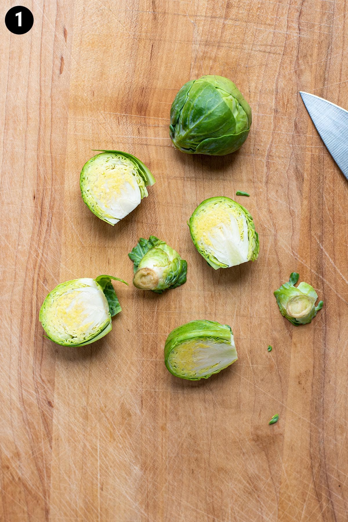 A raw brussels sprout trimmed and slices in half on a wooden cutting board.