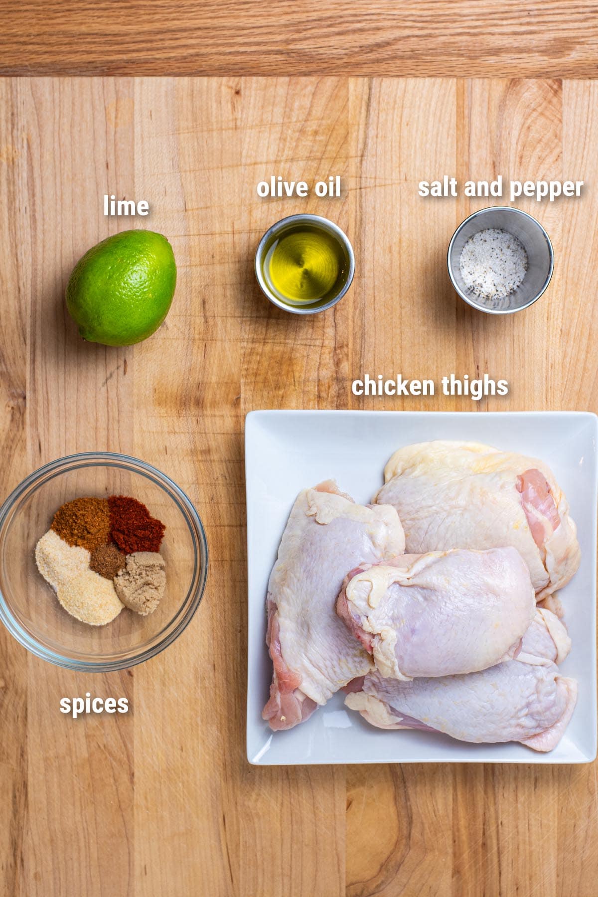 Raw, uncooked chicken thigh ingredients laid out on a wooden cutting board.