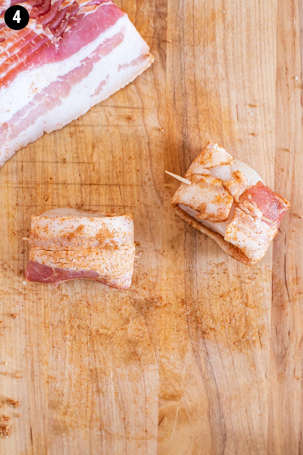 Raw scallops wrapped in uncooked bacon on a wooden cutting board.