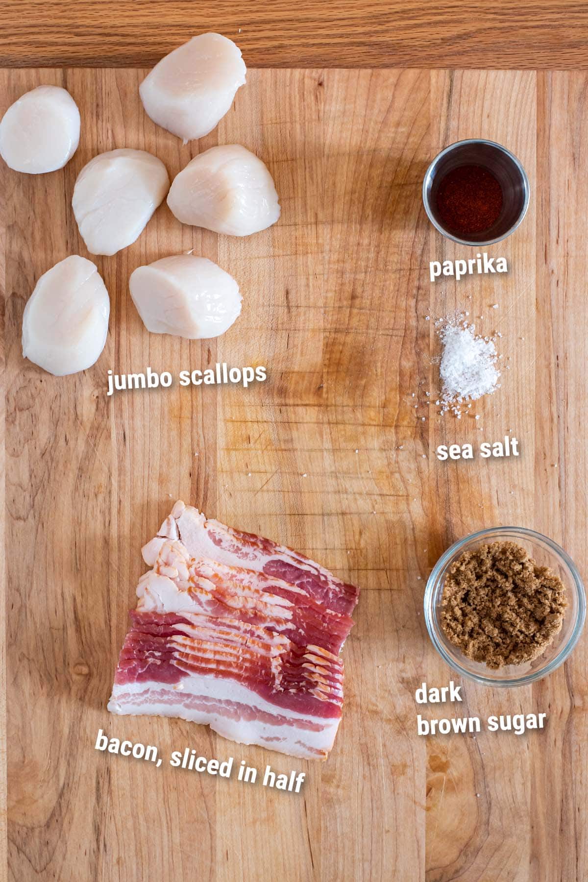 Raw ingredients for bacon wrapped scallops on a wooden cutting board.