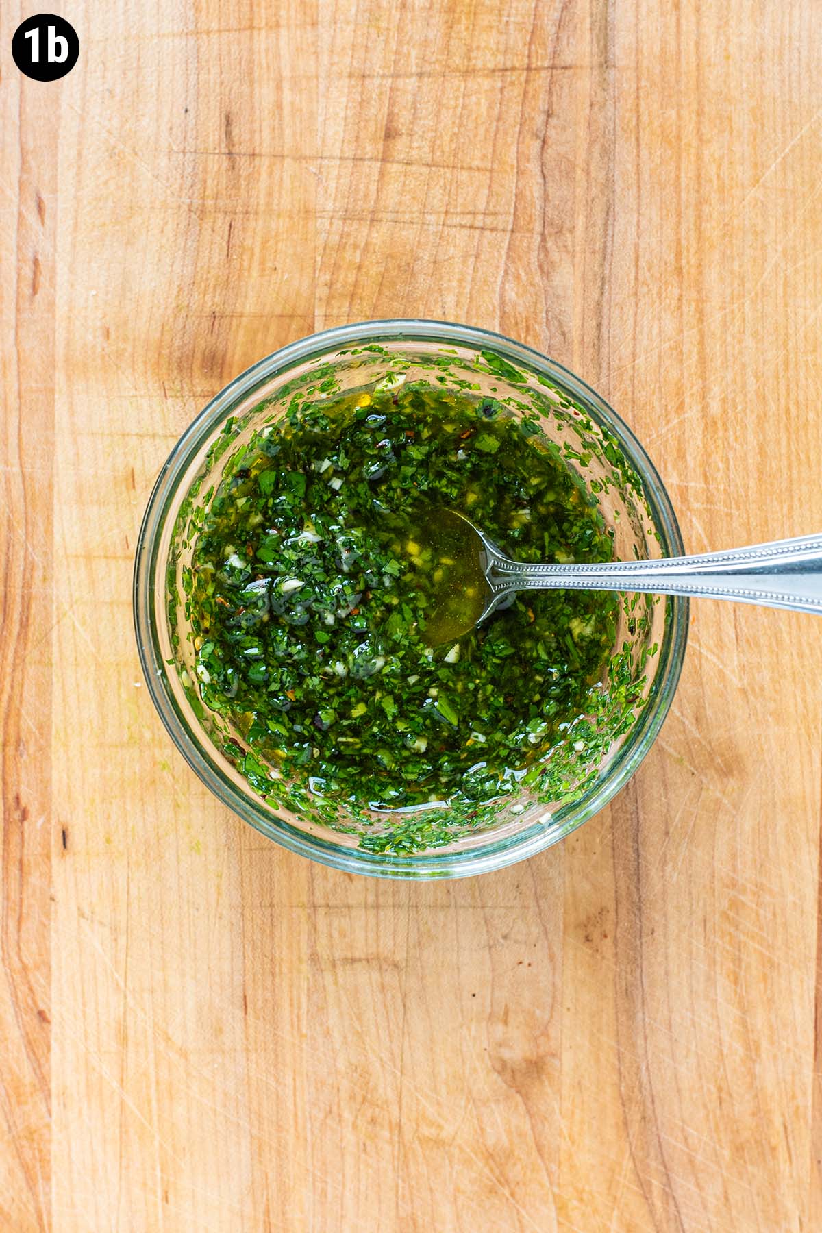 Chimichurri sauce in a small glass bowl on a wooden cutting board.