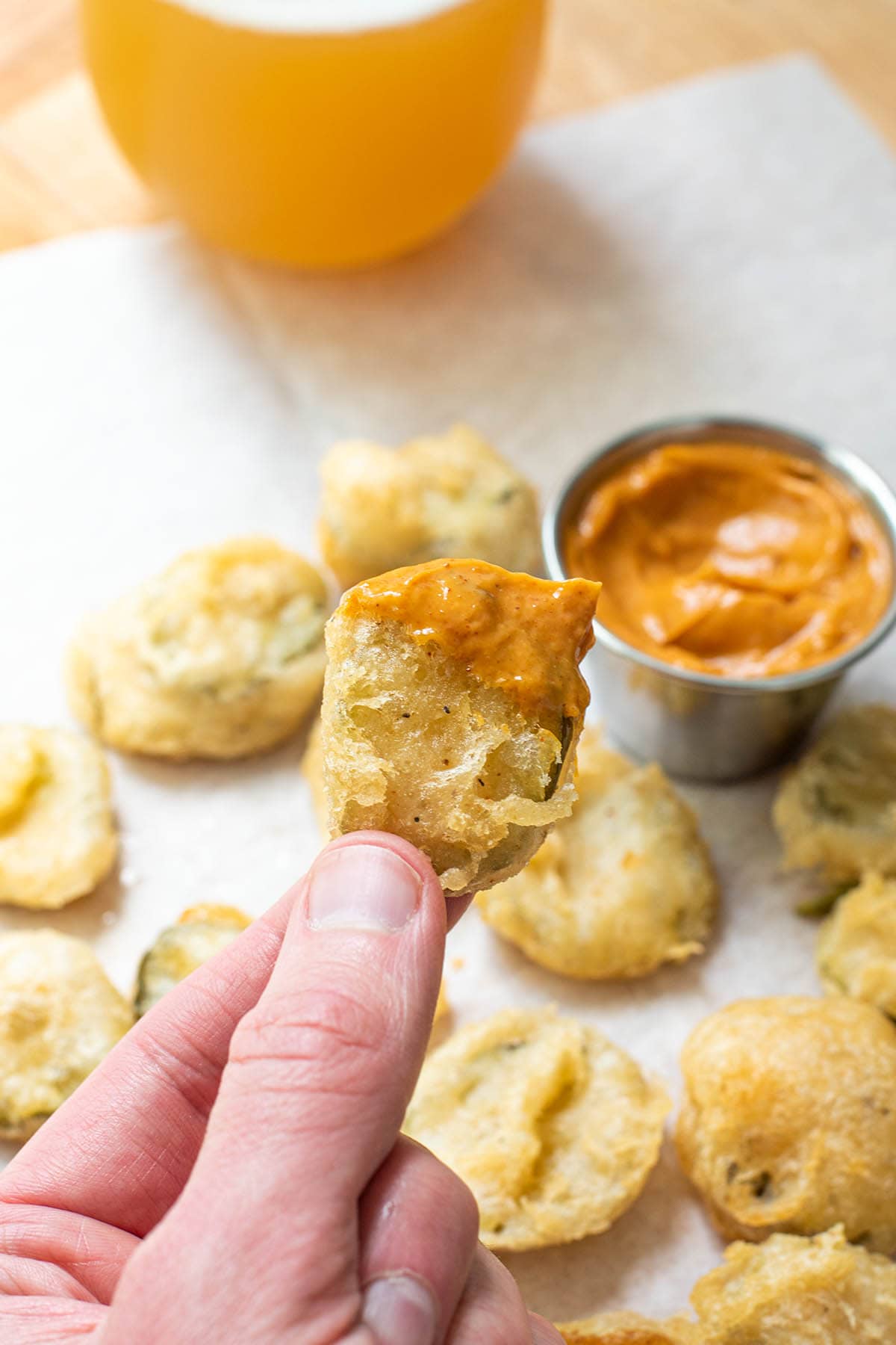 A hand holding a golden fried pickle dipped in chipotle mayo.