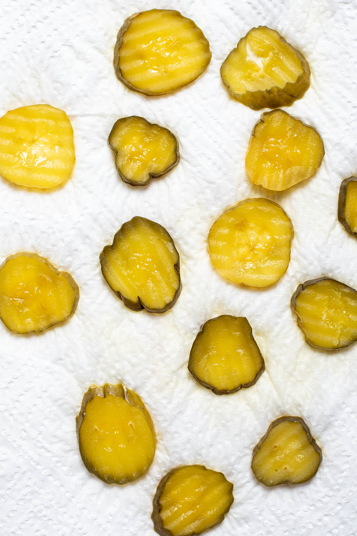 Dill pickle chips draining on a paper towel.