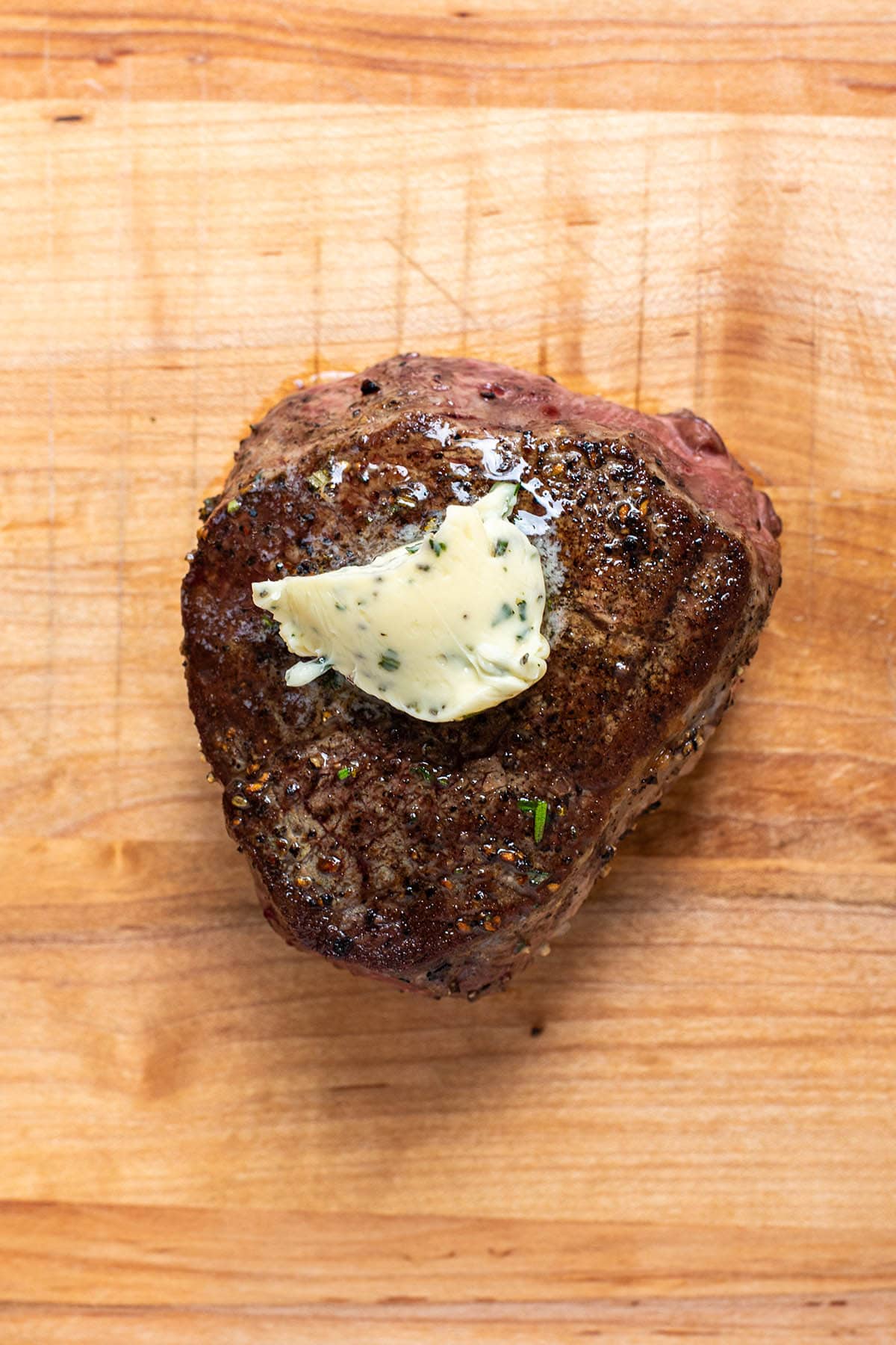 Pan seared filet mignon on a butcher block topped with garlic and herb butter.