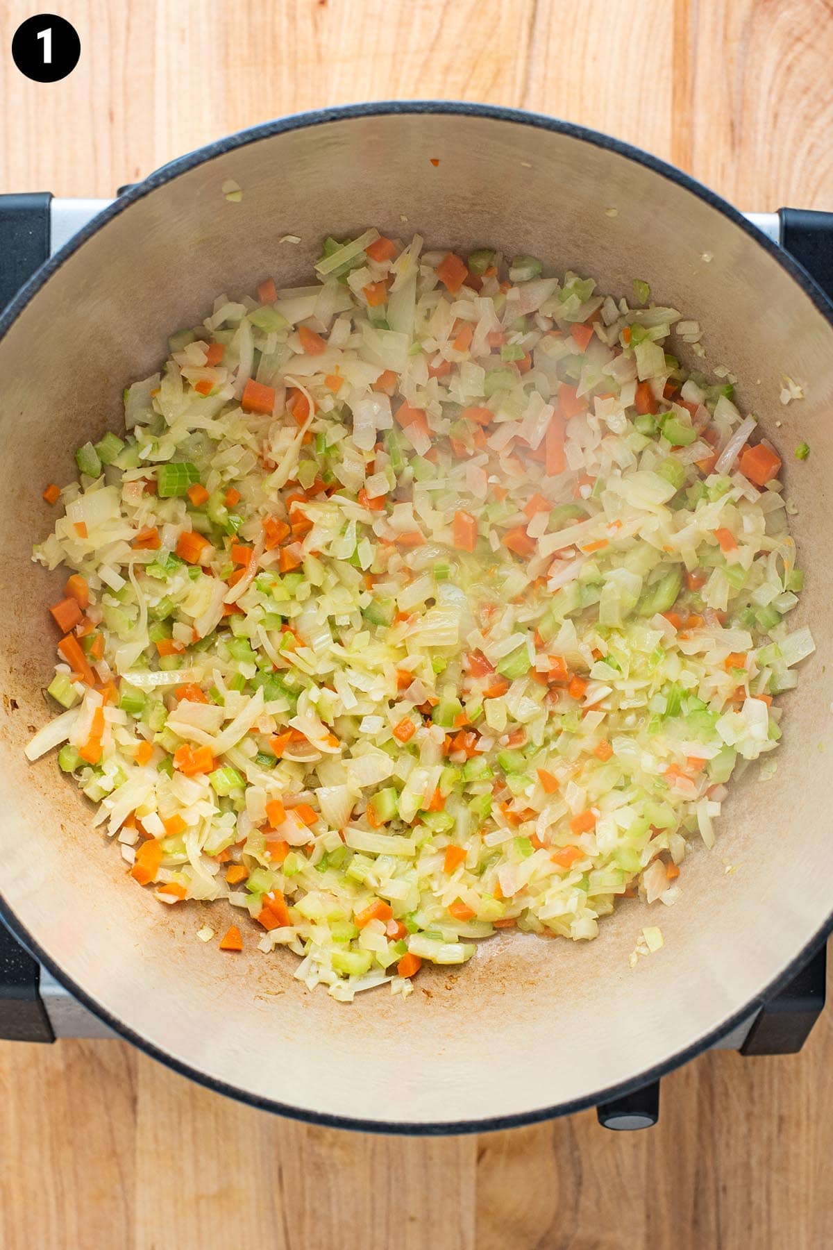 Chopped celery, carrots, onion, and butter simmering in a Dutch oven.