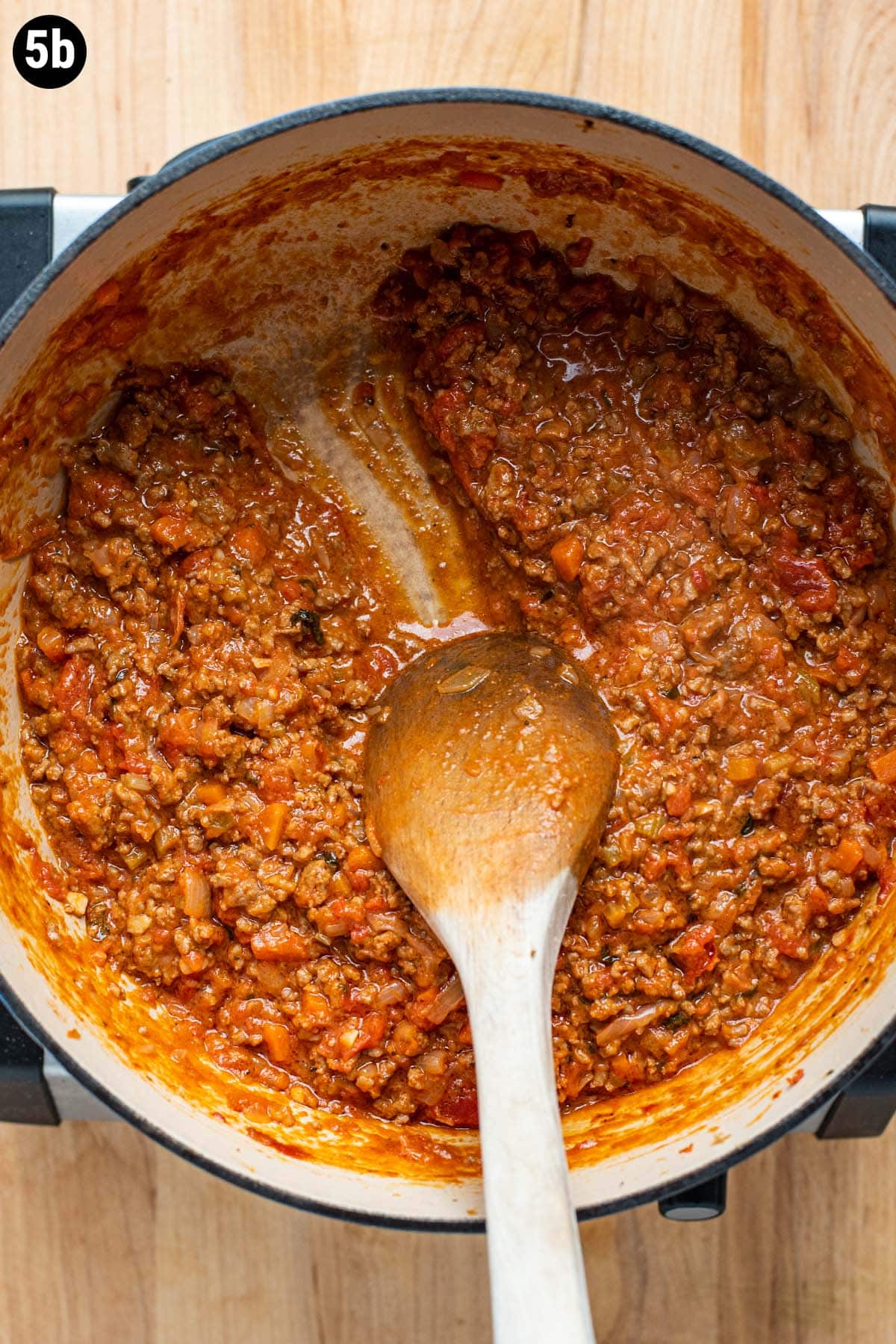 A wooden spoon running through thickened Bolognese sauce.