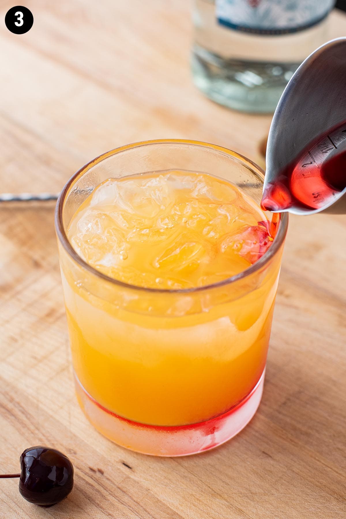 Adding grenadine to a Tequila Sunrise with a cocktail jigger.