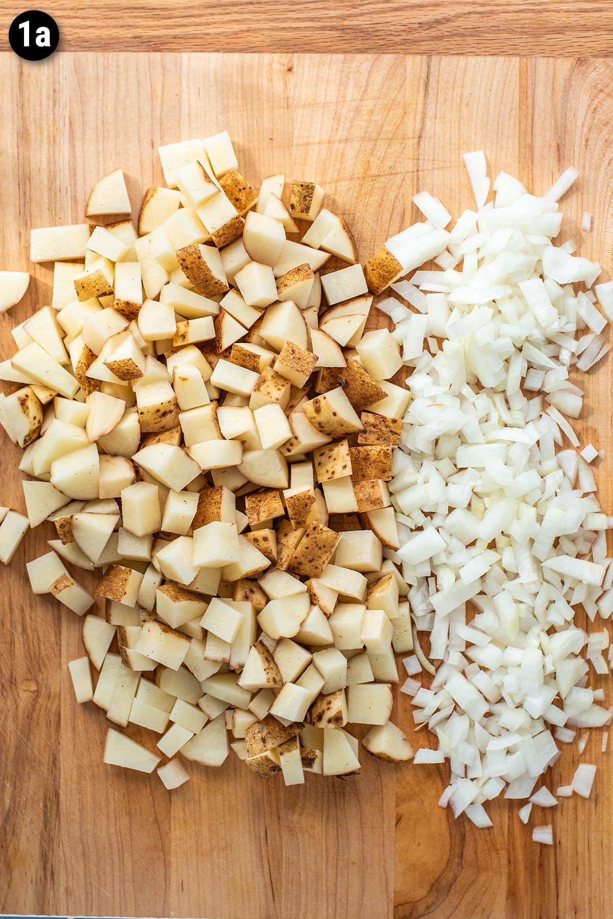 Diced russet potatoes and onions on a wooden cutting board.