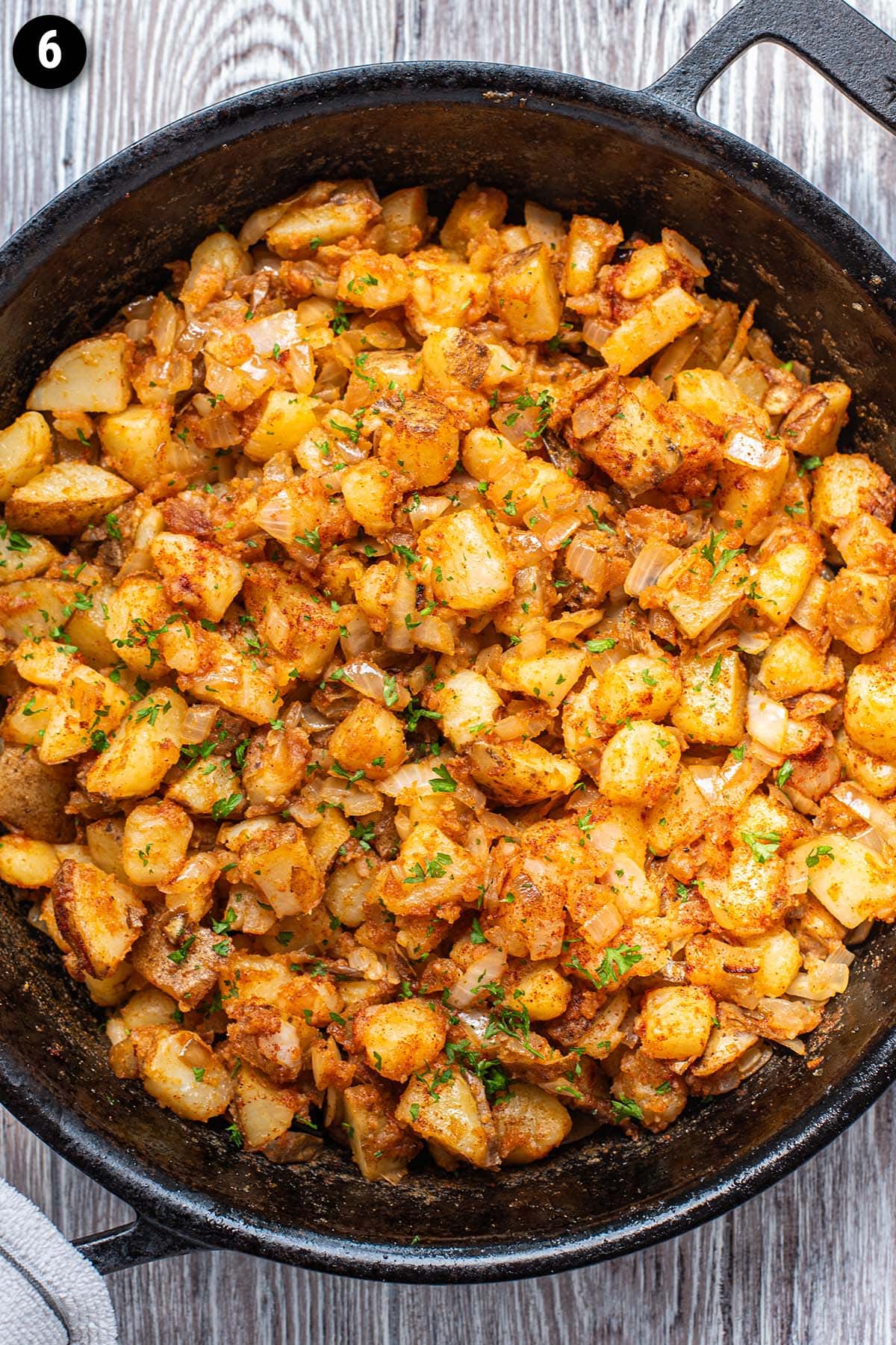 Golden home fries with diced onion and fresh parsley in a cast iron skillet.