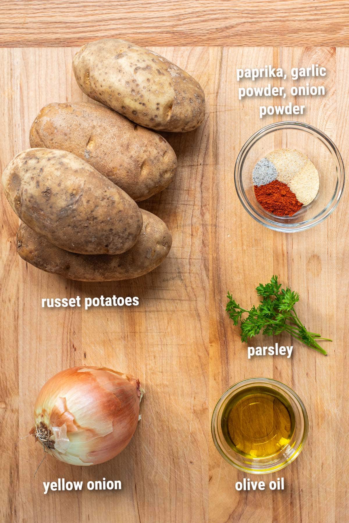 Raw, uncooked home fries ingredients laid out on a wooden cutting board.