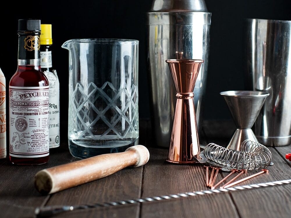 Classic bar tools and cocktail bitters on a wooden table.