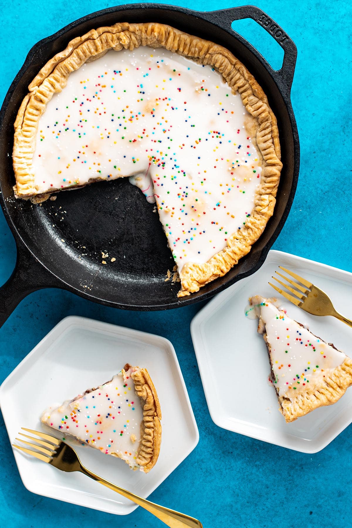 A strawberry skillet Pop Tart in "pie form" with two slices served with forks on small white plates.