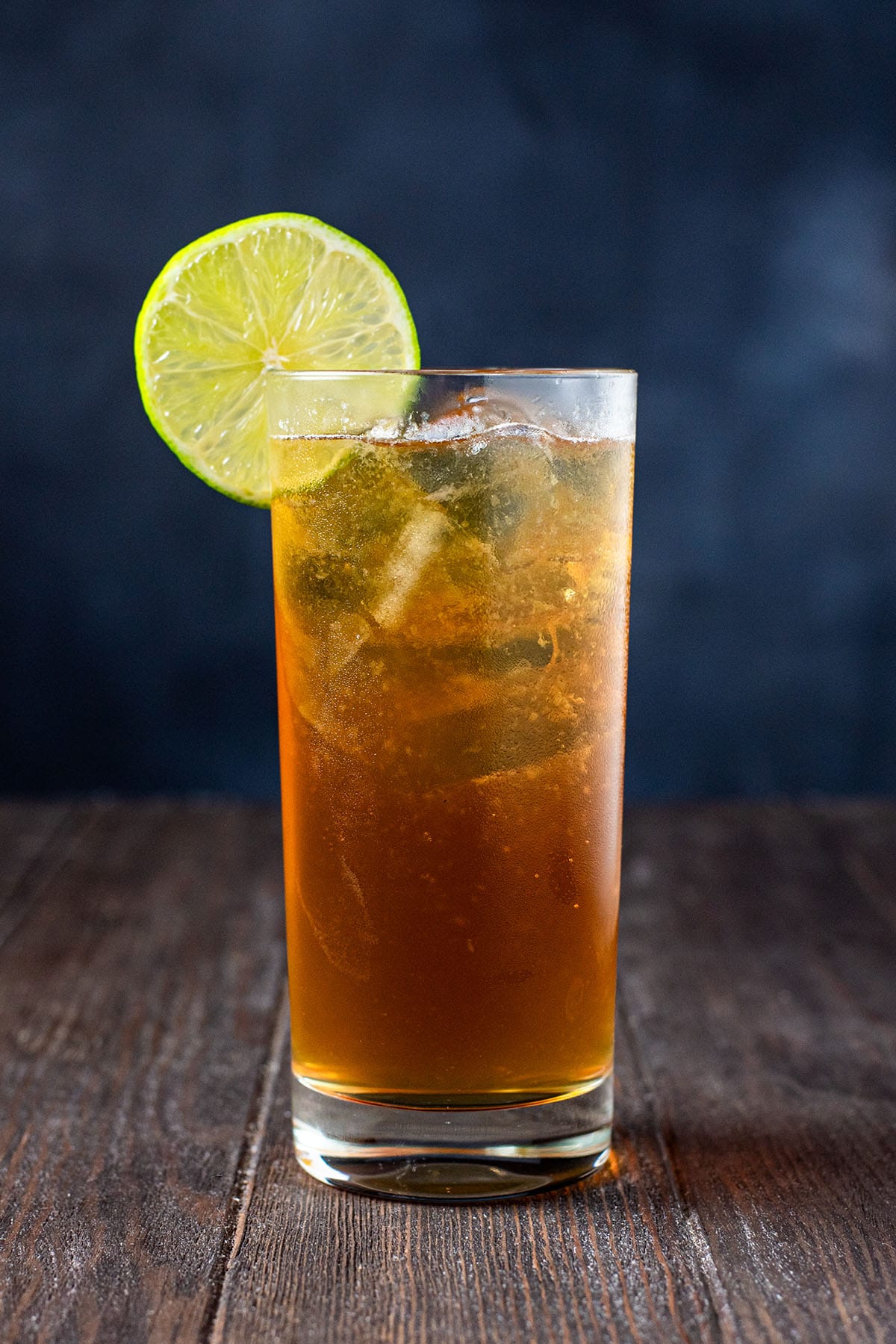 A Dark 'n Stormy cocktail in a highball glass garnished with a lime wheel.