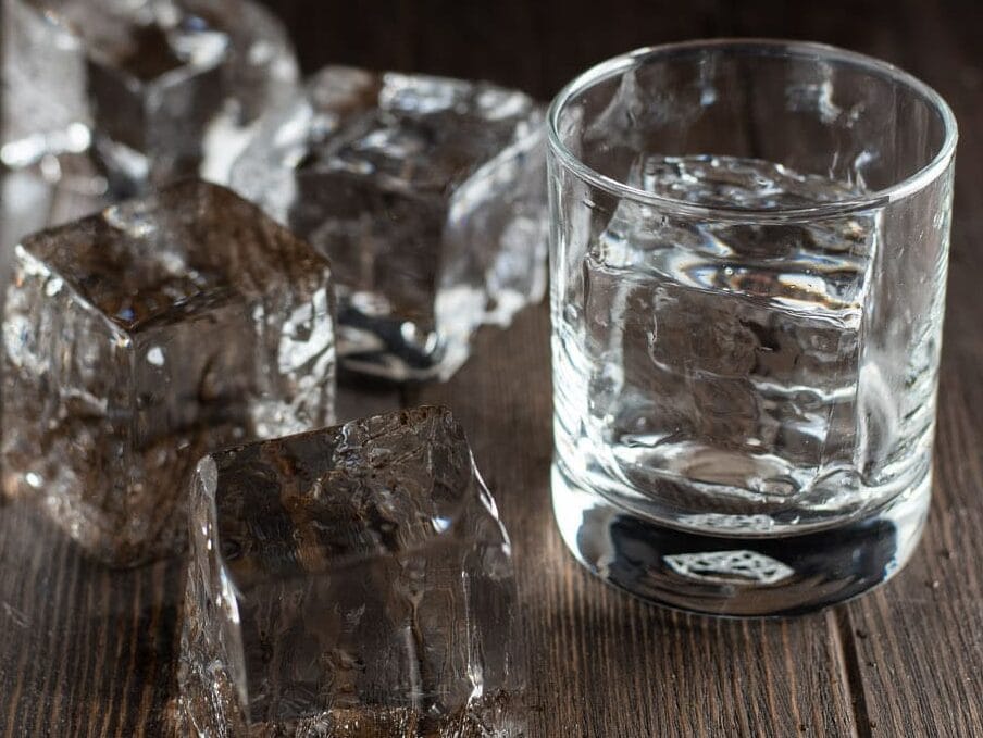 Crystal clear ice cubes on a wooden table and one in a cocktail class.