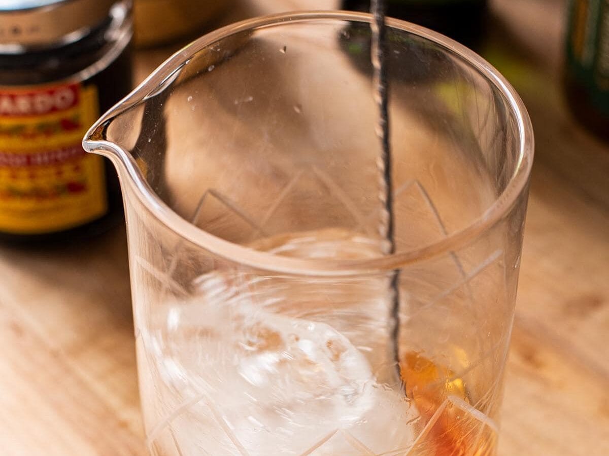 Stirring a whiskey cocktail with ice in a mixing glass.