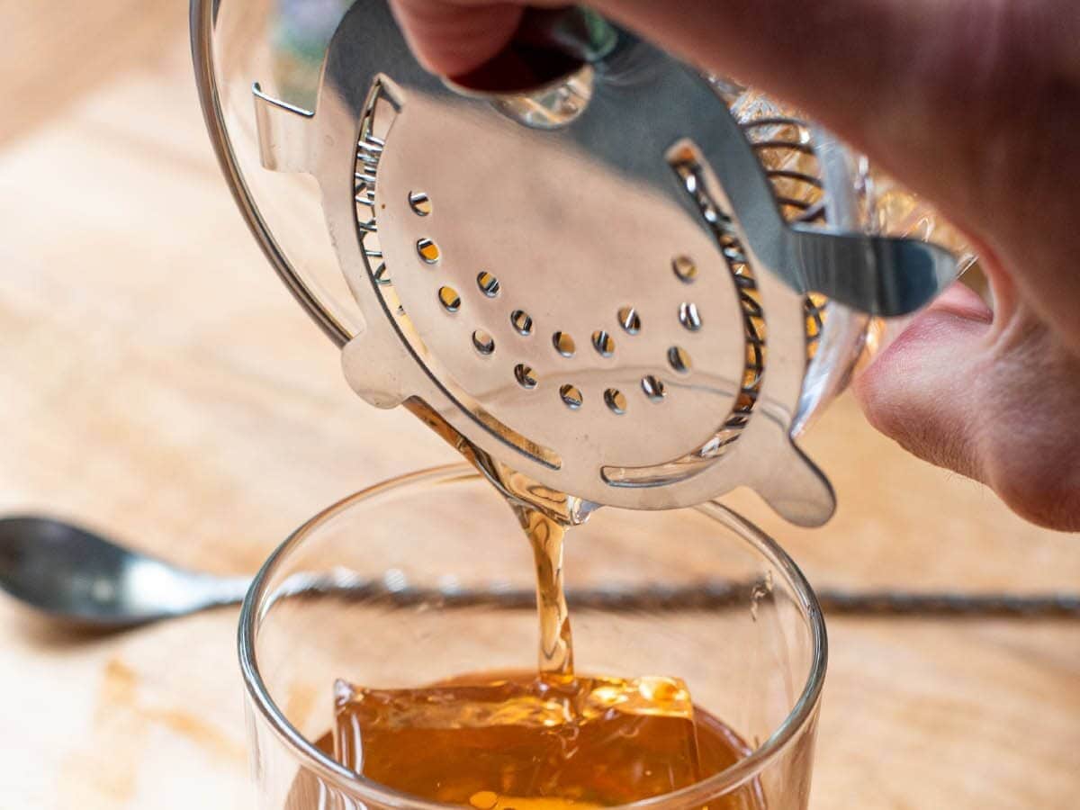 Straining a whiskey cocktail into a glass with a hawthorn strainer.