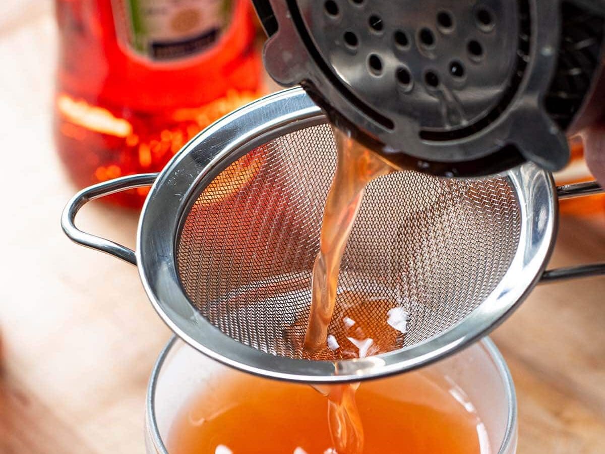 Pouring a cocktail from a shaker through a fine mesh strainer into a coupe glass.