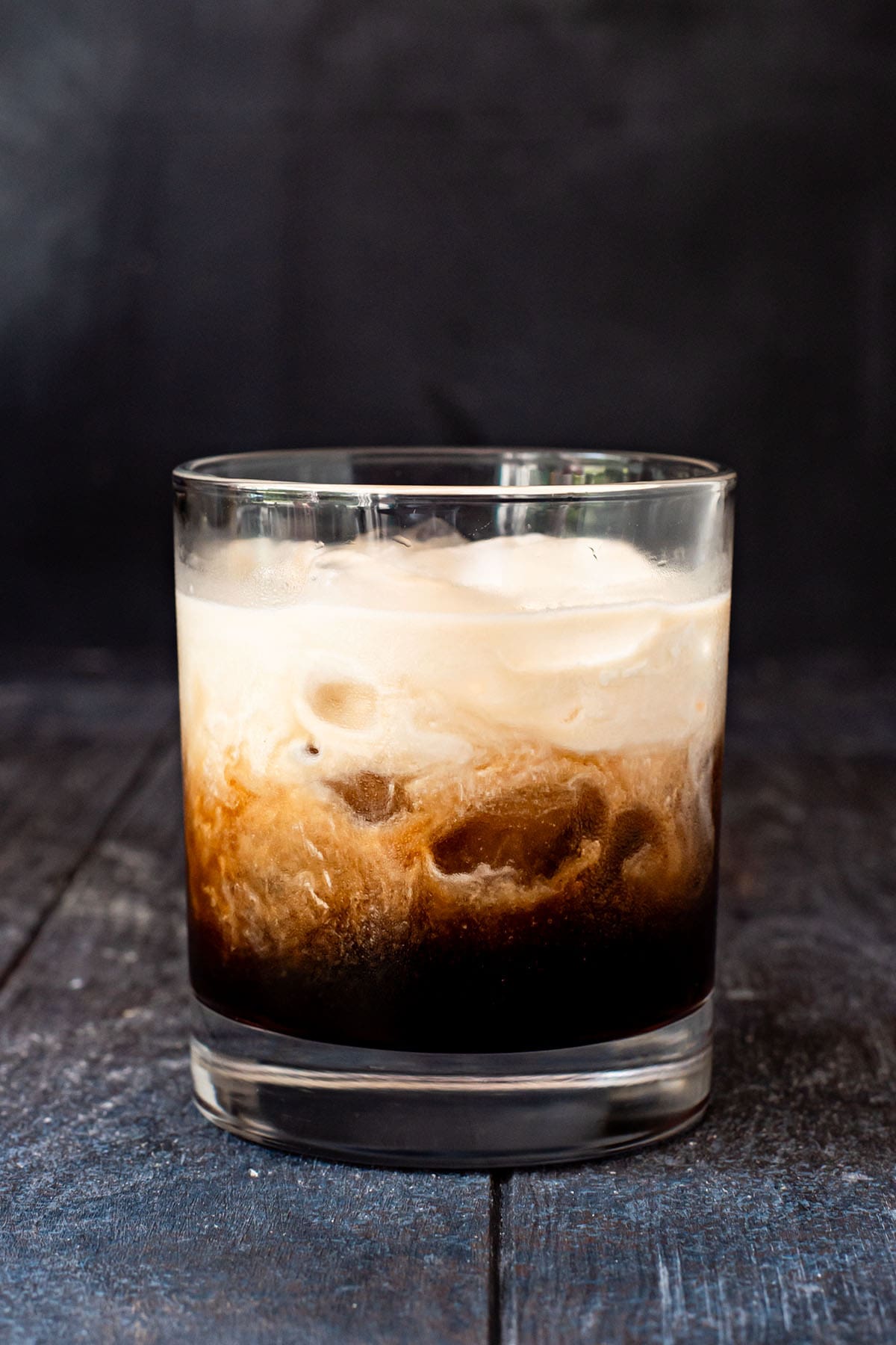 A partially mixed White Russian cocktail topped with heavy cream.