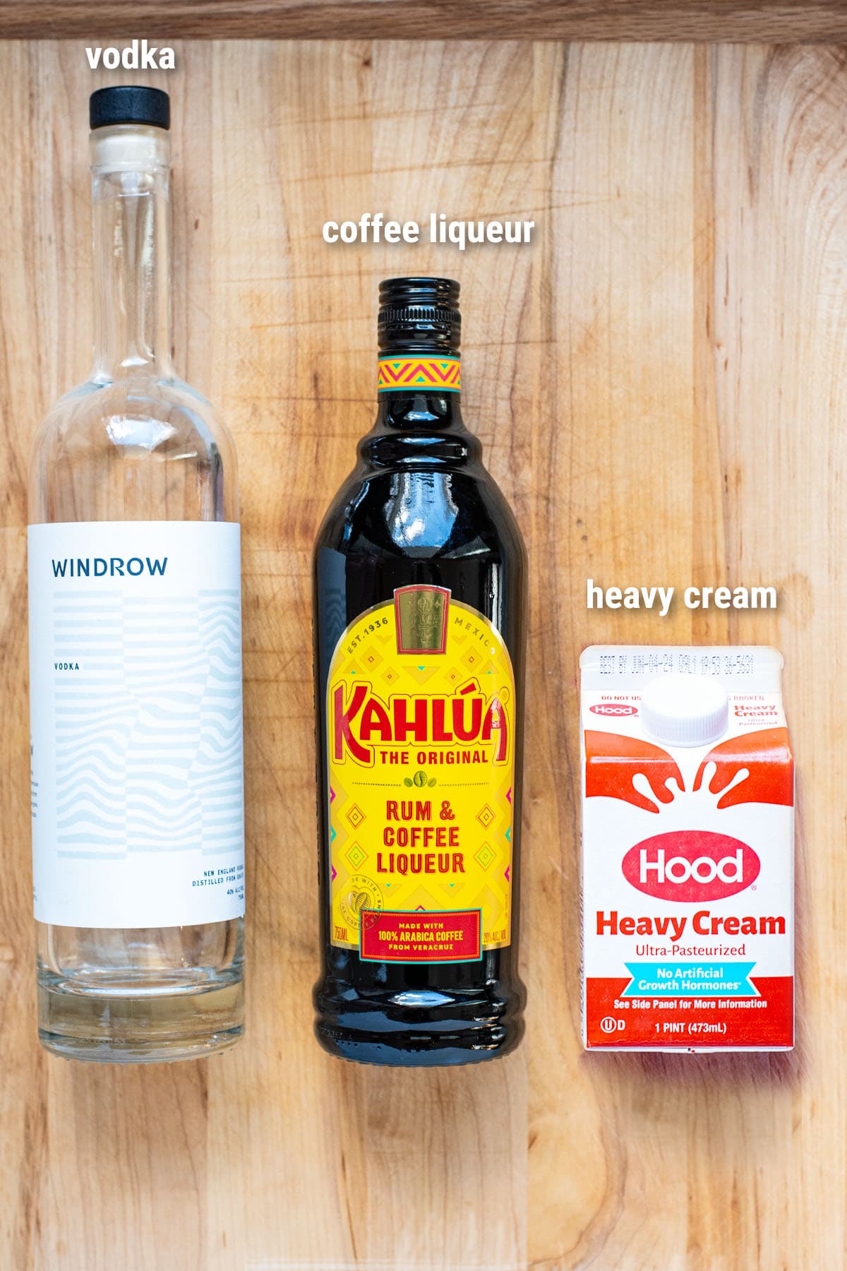 Ingredients for a White Russian cocktail laid out on a wooden cutting board.