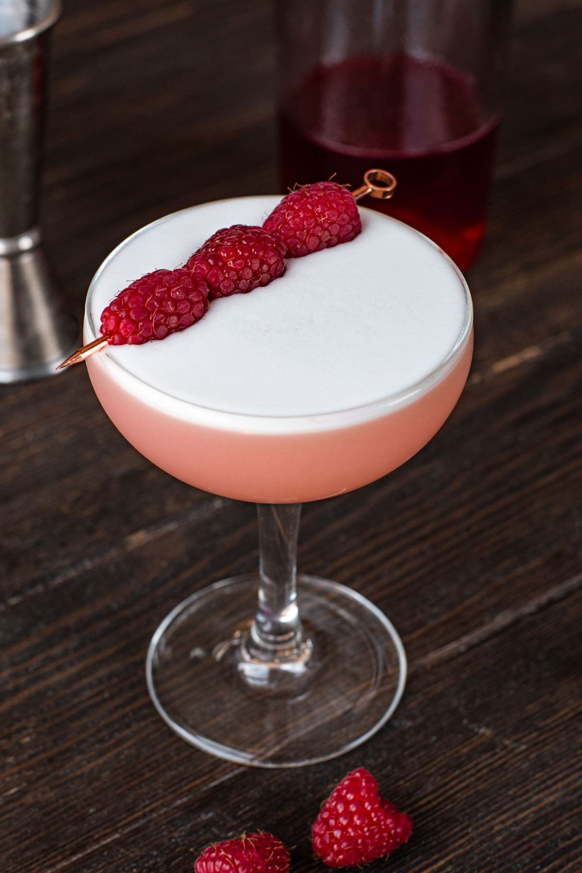 A Clover Club cocktail garnished with three raspberries in a coupe glass.