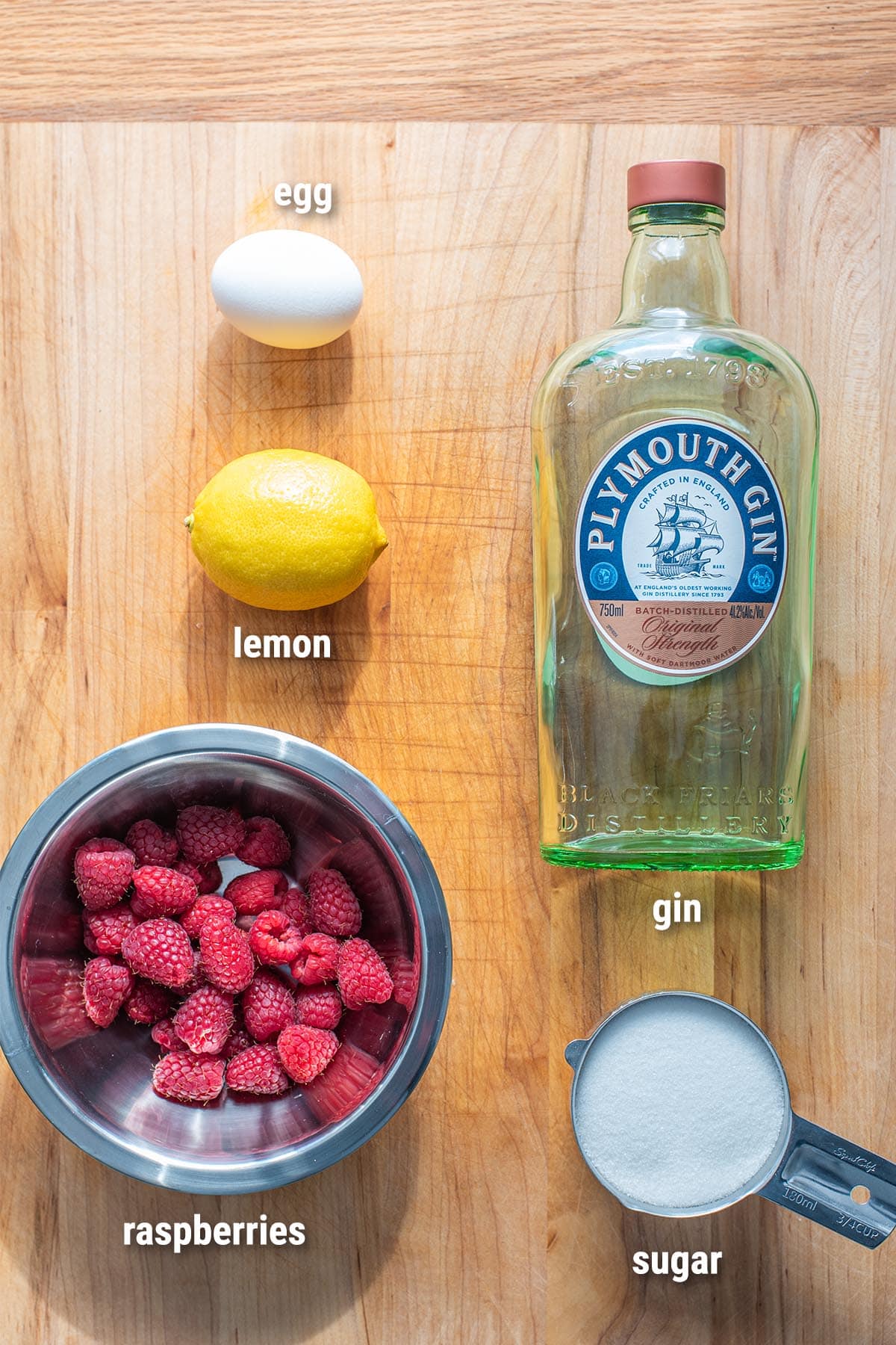 Ingredients for a Clover Club cocktail laid out on a wooden cutting board.