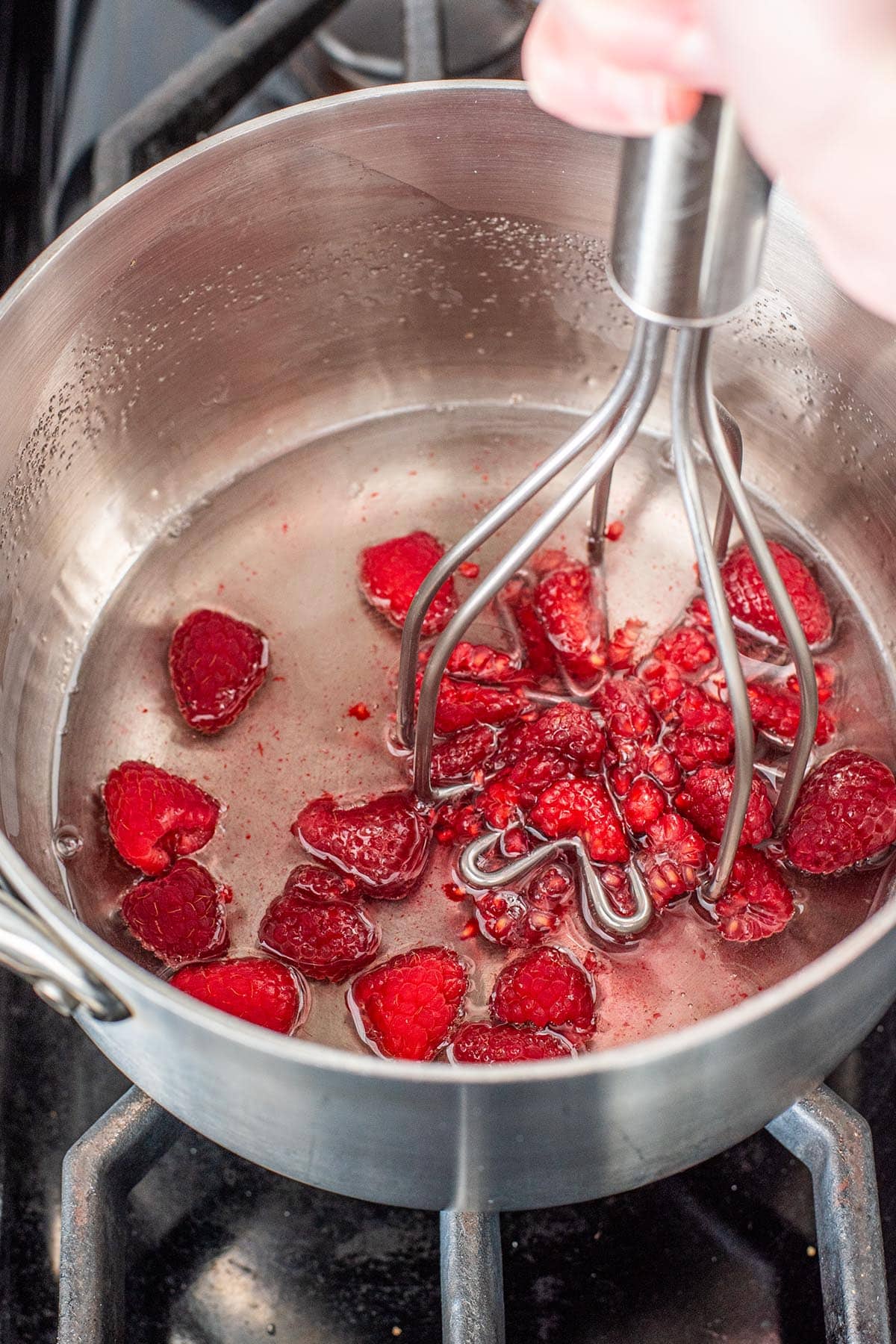 Mashing fresh raspberries in simple syrup in a small saucepan.