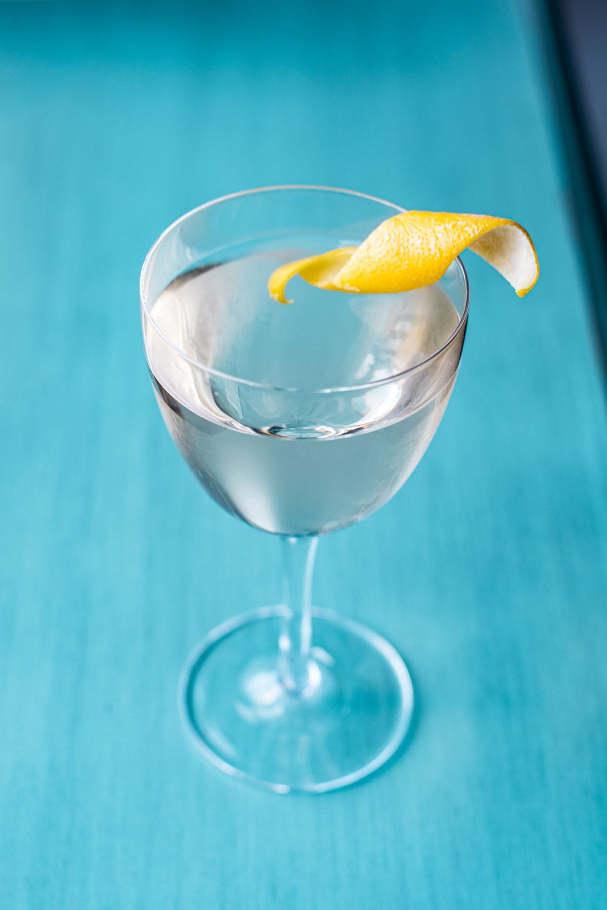 A classic gin Martini garnished with a lemon peel twist on a pale blue surface.