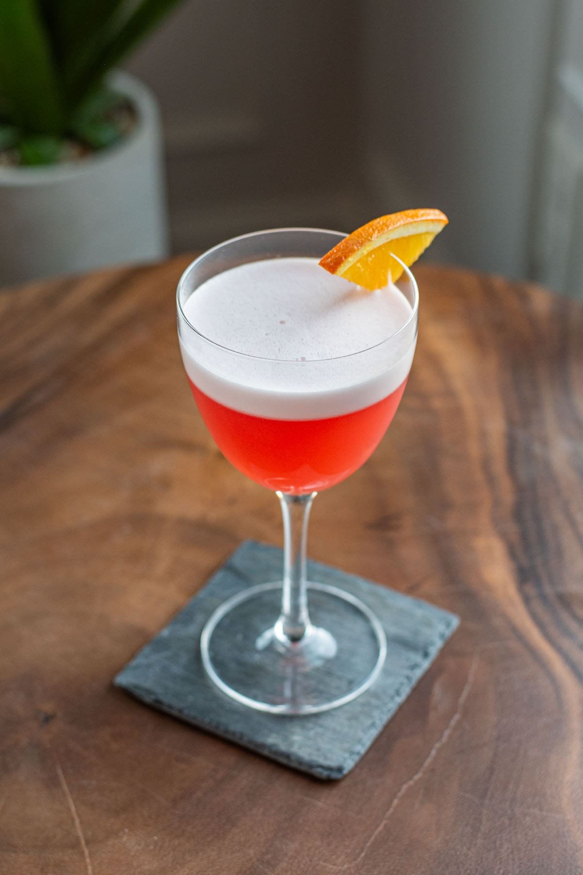 A Mezcal Negroni Sour cocktail with a foamy egg white head and orange wedge garnish.