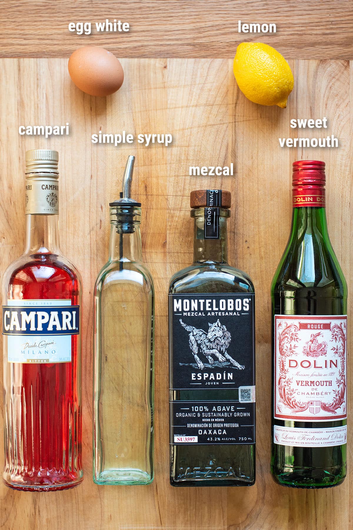 Mezcal Negroni Sour cocktail ingredients laid out on a wooden cutting board.