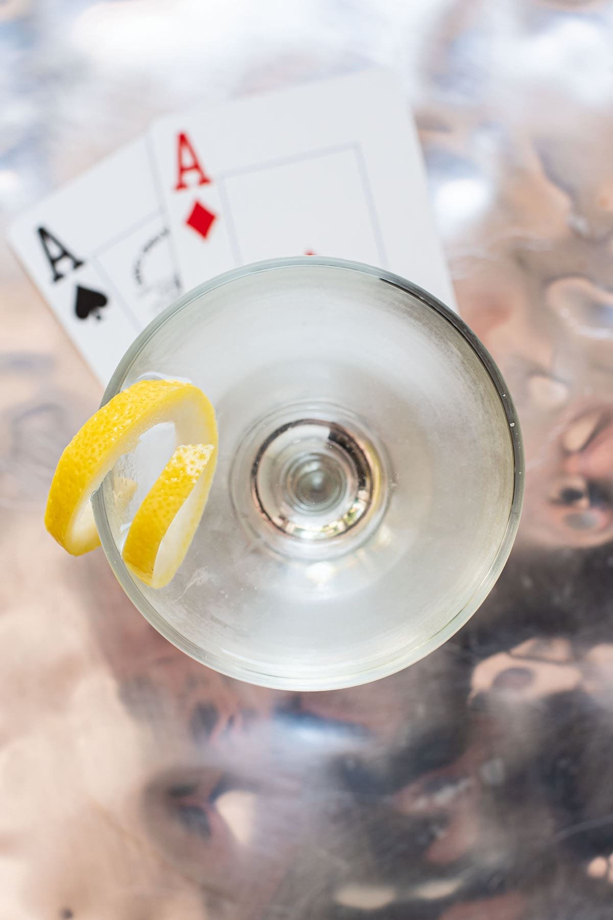 A Vesper Martini with a lemon twist in a coupe glass sitting atop two Ace playing cards.